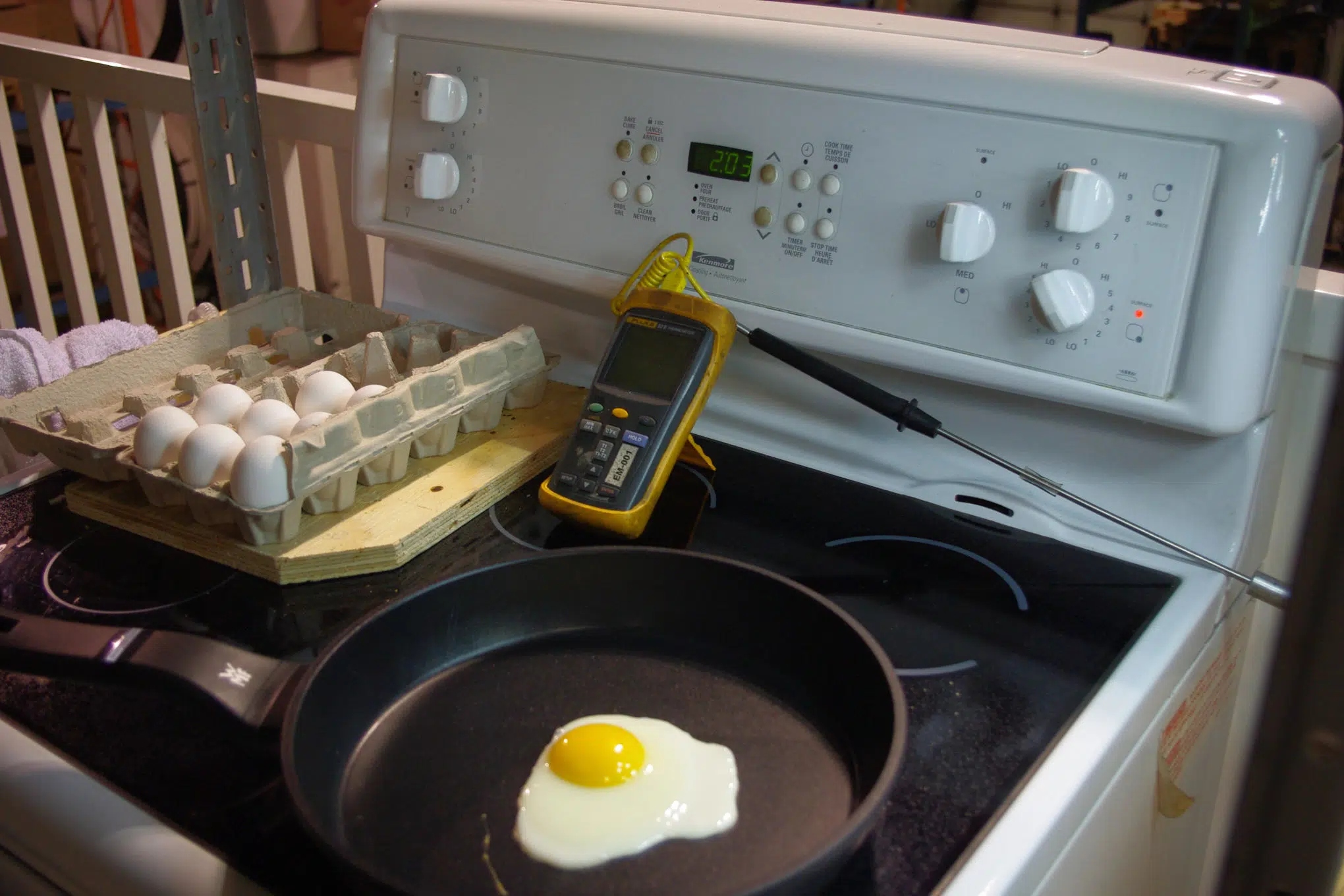 Paistinpannulla paistetaan kananmunaa. Liedellä on myös lämpömittari sekä kananmunakenno.