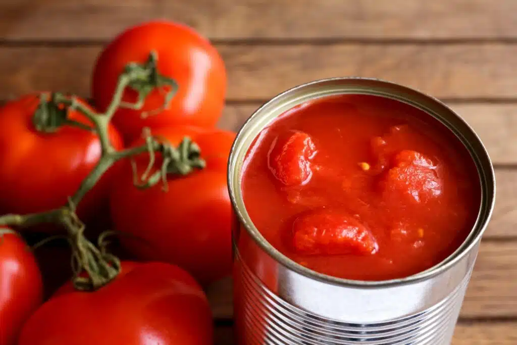Tomaattimurskaa säilykepurkissa. Säilykepurkin vieressä on tomaatteja.