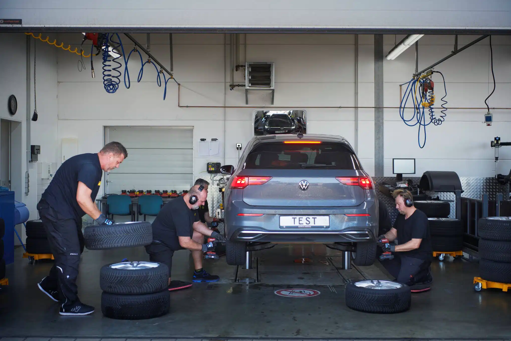 Kolme henkilöä vaihtamassa Volkswagen-merkkisen henkilöauton renkaita.