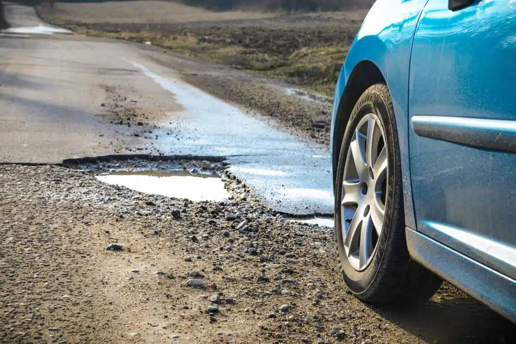 Henkilöauto on tiellä, jossa on reikä.