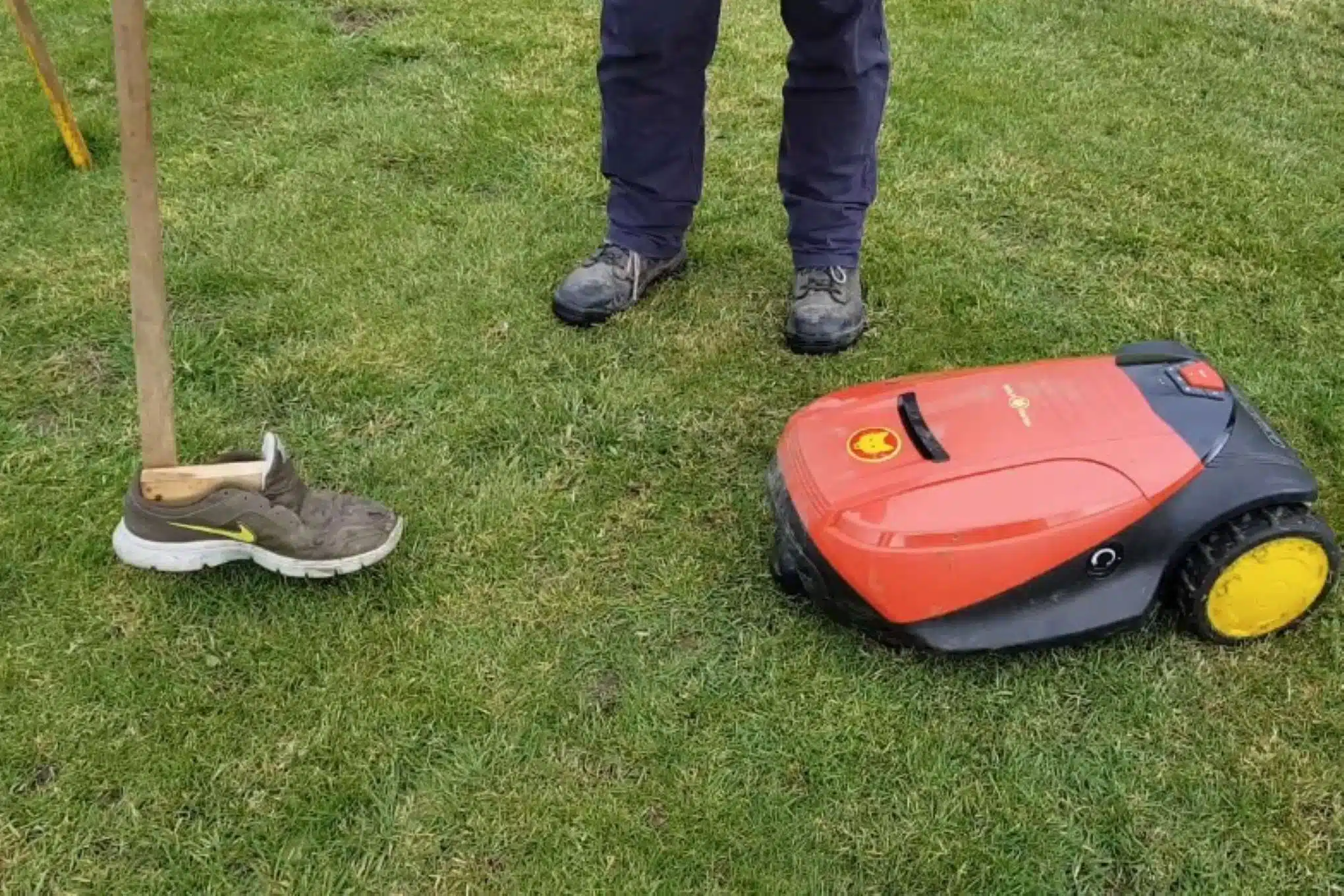 Nurmikolla on henkilö, robottiruohonleikkuri ja testauskalustoa.
