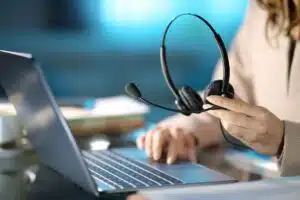 Henkilö, jolla on kädessään kuulokkeet, istuu tietokoneen ääressä.